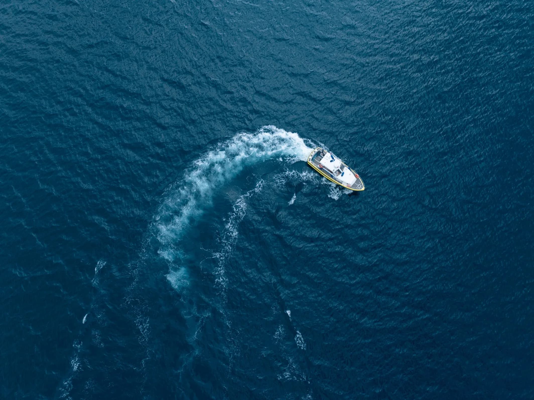 Veduta aerea di una motovedetta che accosta lasciando una scia curva sul mare aperto