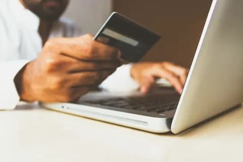 Una persona con la carta di credito in mano davanti al portatile, mentre sottoscrive l’abbonamento